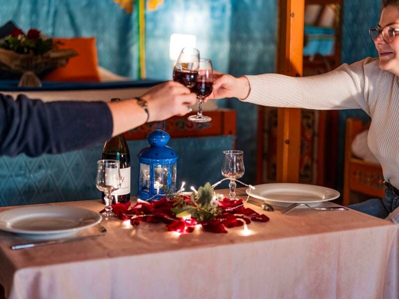 Deux personnes trinquent avec des verres de vin rouge autour d'une table décorée avec des bougies et des fleurs.