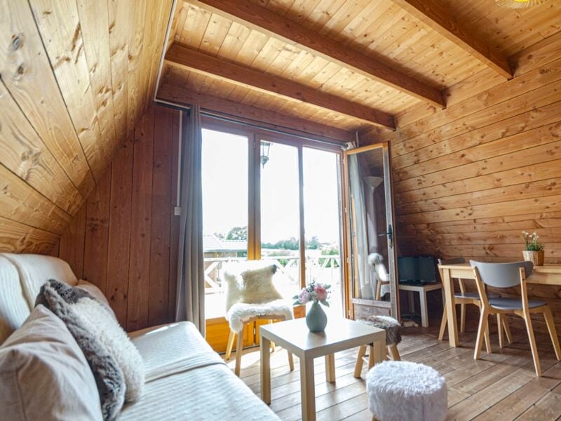 Salon en bois avec canapé, table basse, fauteuil et grande fenêtre donnant sur une terrasse extérieure.