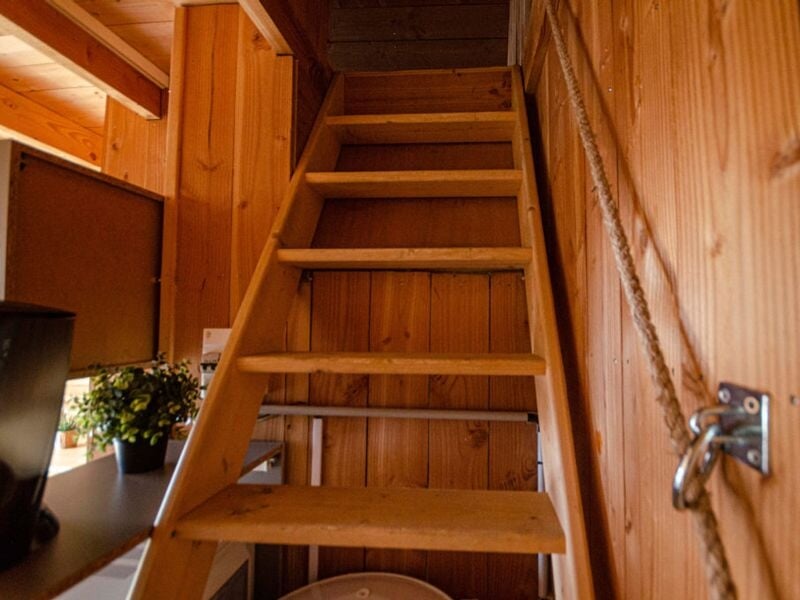 Escalier en bois menant à l'étage supérieur dans une petite cabane en bois aux murs inclinés.