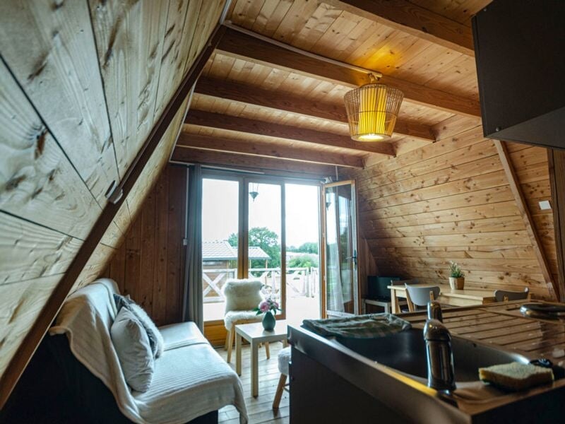 Salon en bois avec canapé, table basse, fauteuil et grande porte-fenêtre ouverte sur l'extérieur.