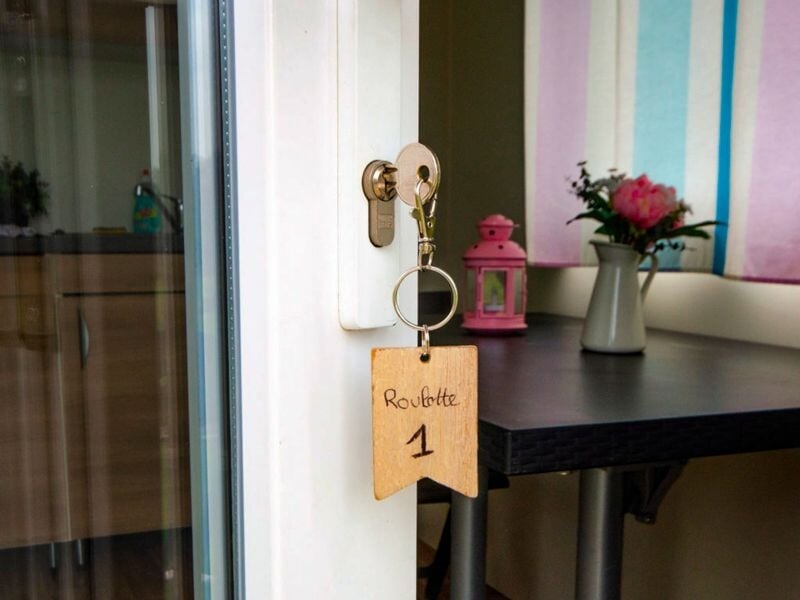 Porte vitrée avec clé insérée dans la serrure et porte-clé en bois marqué 'Roulotte 1', intérieur décoré.