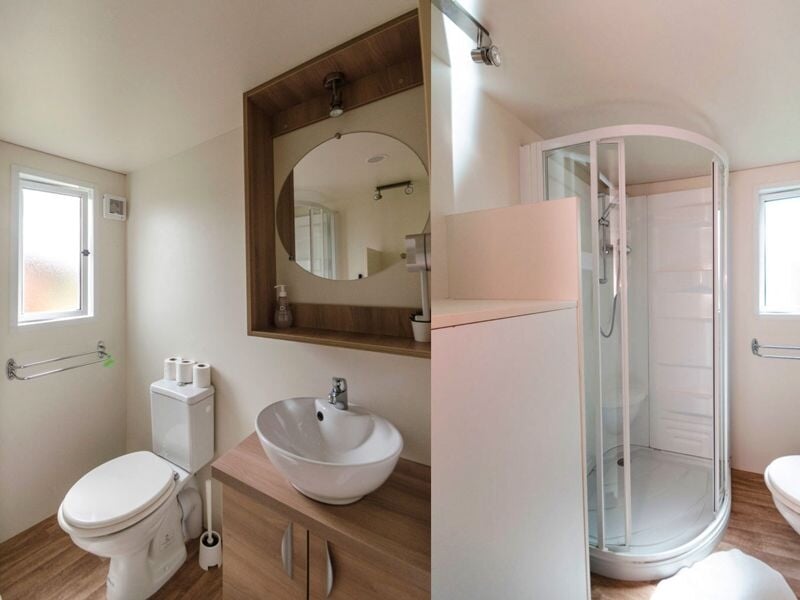 Salle de bain moderne avec lavabo, miroir rond, toilettes et cabine de douche, murs blancs et bois clair.