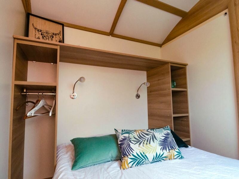 Autre angle de la chambre montrant un canapé vert avec plusieurs coussins colorés et rideaux rayés.