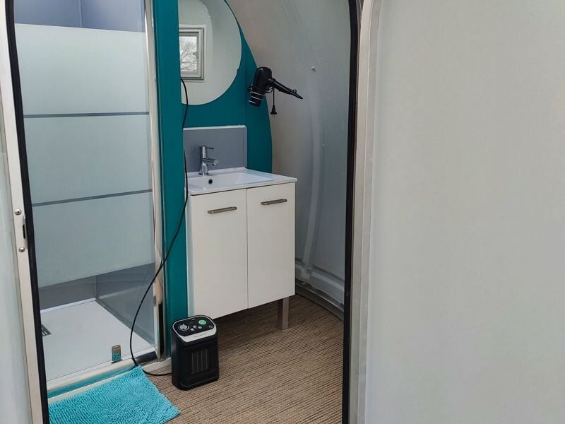 Intérieur d'une bulle avec un meuble lavabo blanc, un miroir et un petit chauffage au sol.