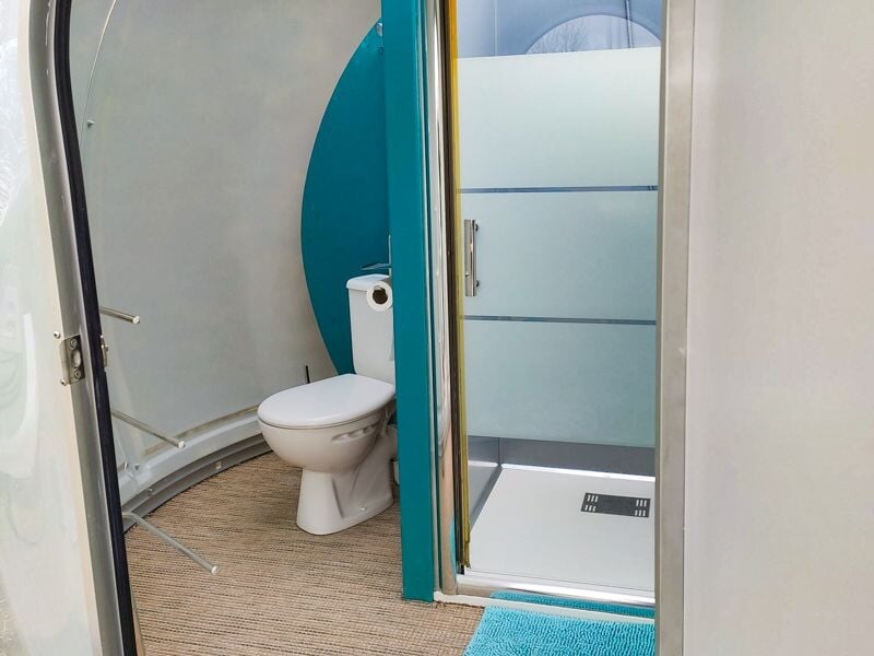 Intérieur d'une bulle avec des toilettes, une douche et un tapis bleu clair au sol.