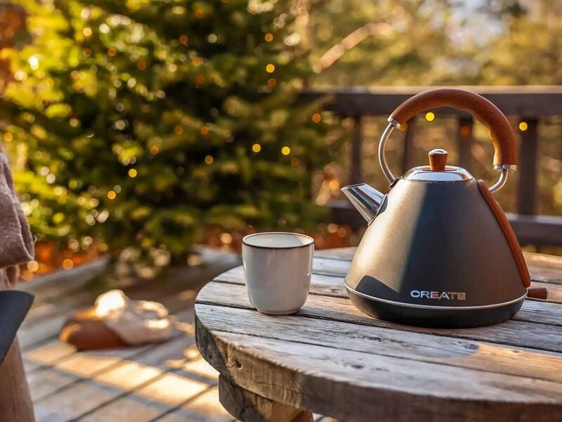 Bouilloire et tasse posées sur une table ronde en bois sur une terrasse avec un sapin décoré.
