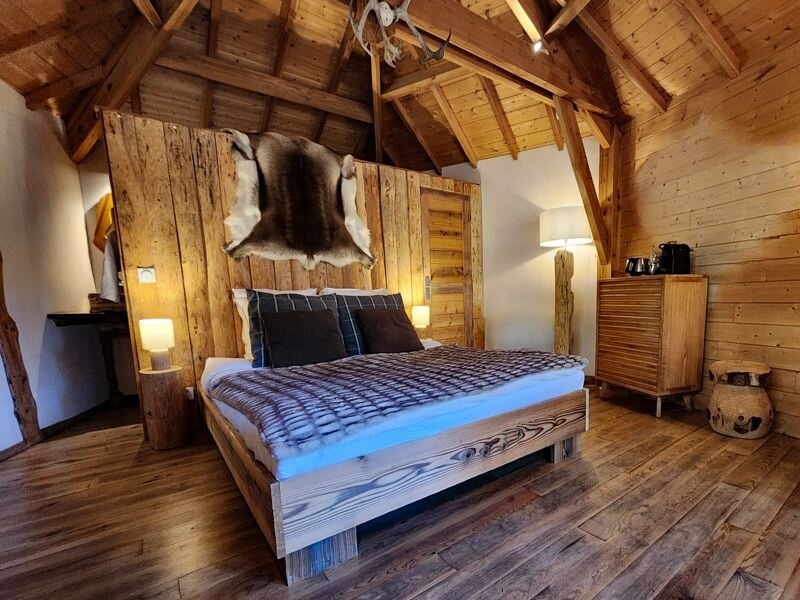 Chambre rustique en bois avec un lit double, une peau d'animal accrochée au mur et une lampe.