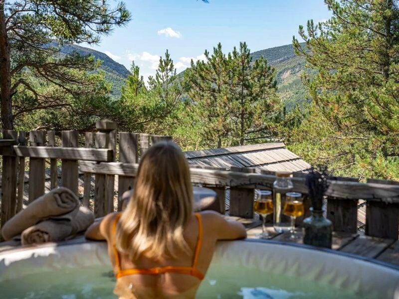 Femme dans un jacuzzi extérieur entouré d'arbres, profitant d'une vue sur la montagne.