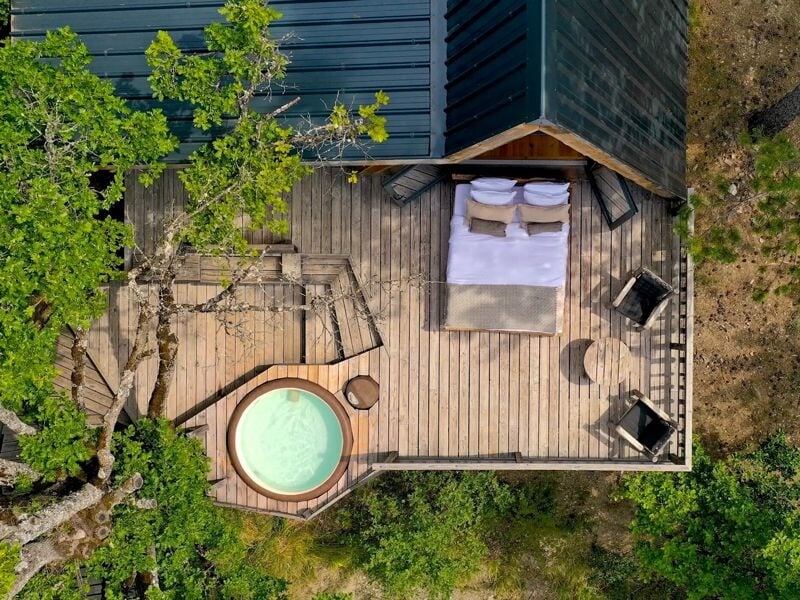 Vue aérienne d'une terrasse en bois avec un jacuzzi, un lit double et deux fauteuils.