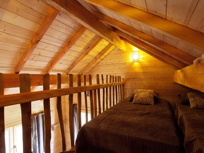 Intérieur d'une mezzanine en bois avec un lit double et une lumière douce créant une ambiance chaleureuse.