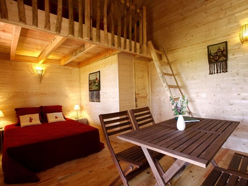 Pièce en bois avec un lit double rouge, une table en bois et des chaises, décor rustique et cosy.