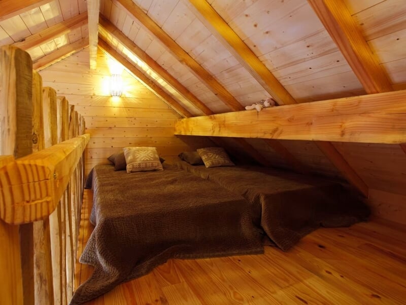Mezzanine en bois avec lit double et lumière tamisée, ambiance intime et confortable.
