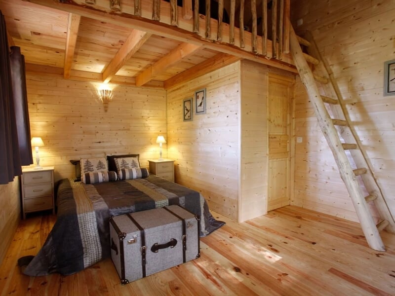 Chambre en bois avec lit double, mezzanine accessible par une échelle, ambiance chaleureuse.
