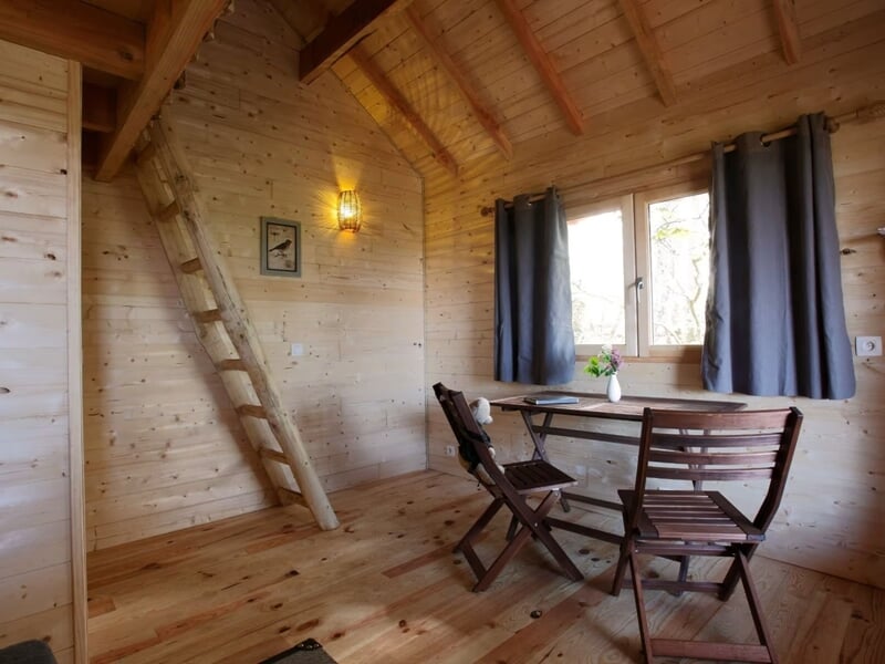 Pièce en bois avec table et chaises, fenêtre avec rideaux gris, ambiance simple et lumineuse.