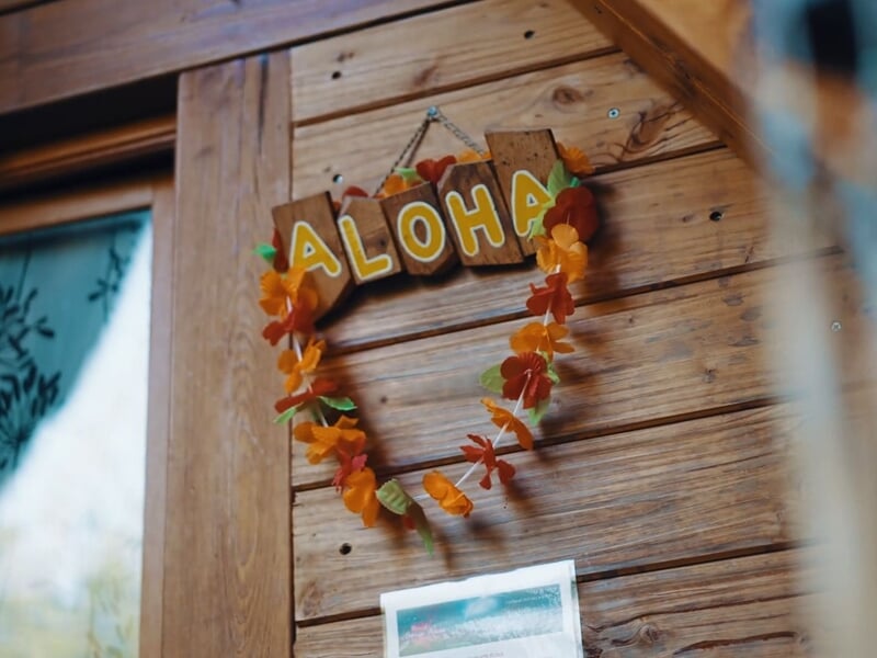 Pancarte en bois avec inscription ALOHA et guirlande de fleurs tropicales suspendue sur un mur en bois.