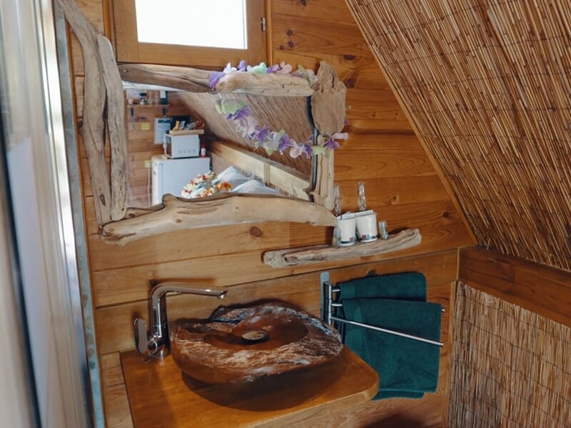 Salle de bain rustique avec lavabo en bois sculpté, miroir encadré de bois et serviettes vertes.