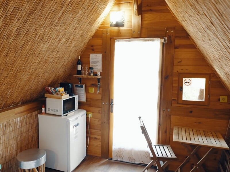 Coin cuisine avec réfrigérateur, micro-ondes, table pliante et chaise dans une pièce en bois clair.