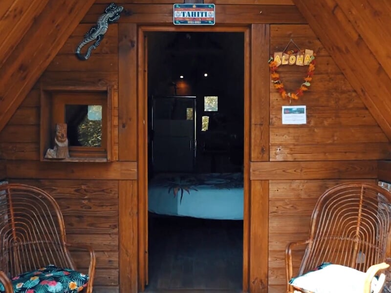 Entrée d'une cabane en bois avec deux fauteuils en rotin et décoration murale tropicale.
