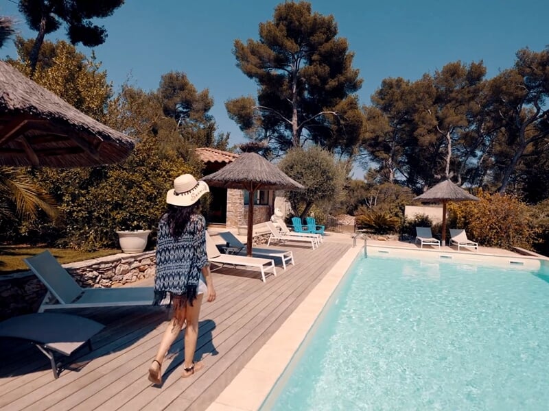 Femme marchant près d'une piscine entourée de chaises longues et parasols sous un ciel bleu.