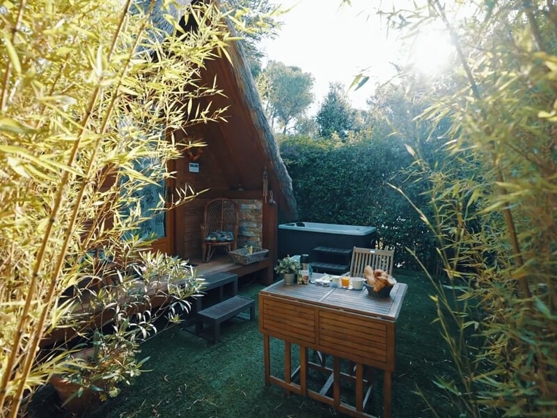 Petit jardin ensoleillé avec table en bois, chaises et cabane en bois entourée de bambous.