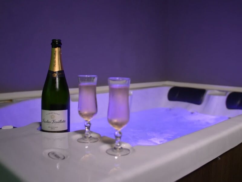Bouteille de champagne et deux flûtes posées sur le bord d'un jacuzzi éclairé en violet.