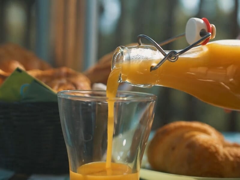 Verre posé sur une table avec du jus d'orange fraîchement versé depuis une bouteille en verre.