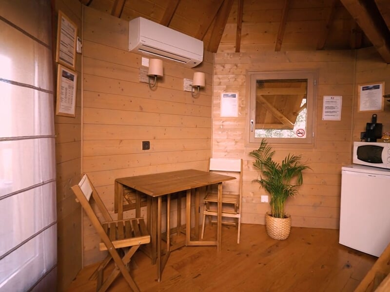 Coin repas dans une cabane en bois avec table, chaises, plante verte et électroménager blanc.