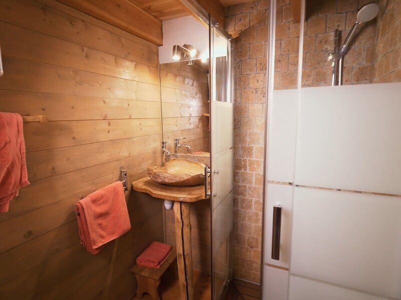 Salle de bain en bois avec lavabo en bois, miroir, douche vitrée et serviettes orange accrochées.