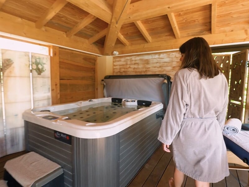 Femme en peignoir blanc entrant dans une pièce avec un grand jacuzzi intérieur moderne.