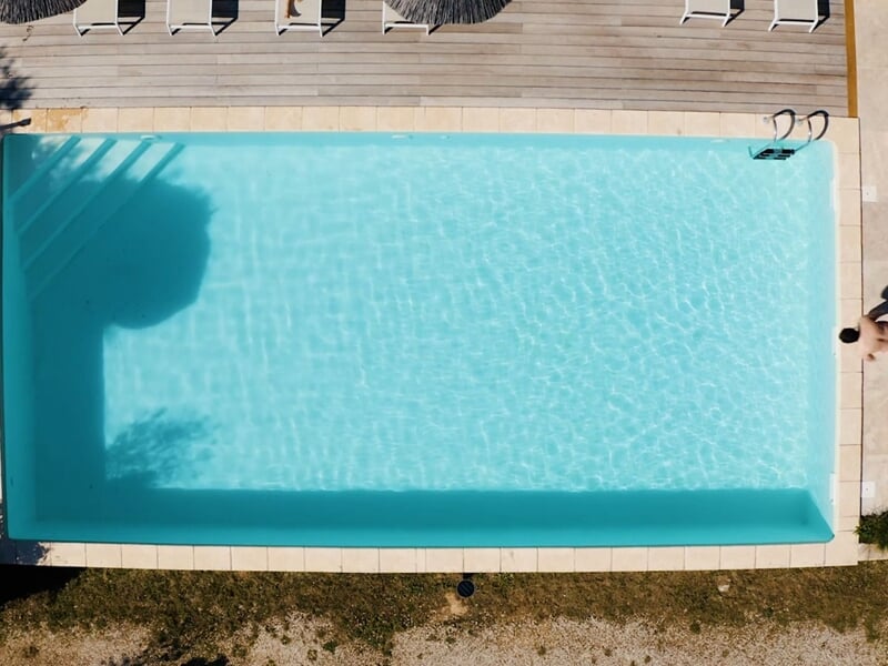 Piscine extérieure rectangulaire avec eau claire et terrasse en bois, vue prise d'en haut.