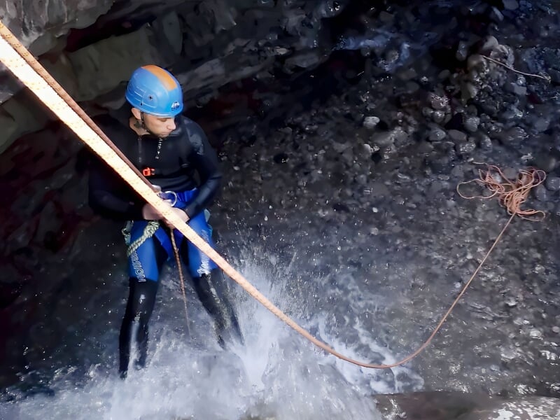 Personne en canyoning descendant une cascade d'eau dans un environnement naturel rocheux