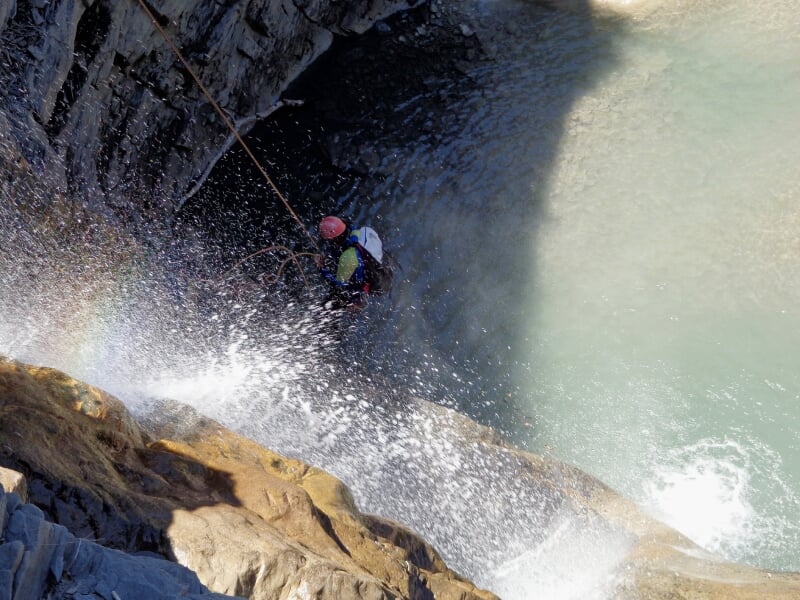 Personne en canyoning descendant une cascade d'eau dans un environnement naturel rocheux