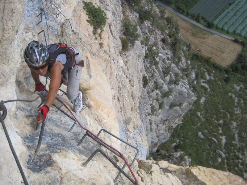 Personne en train de grimper sur une via ferrata avec un casque et un harnais de sécurité