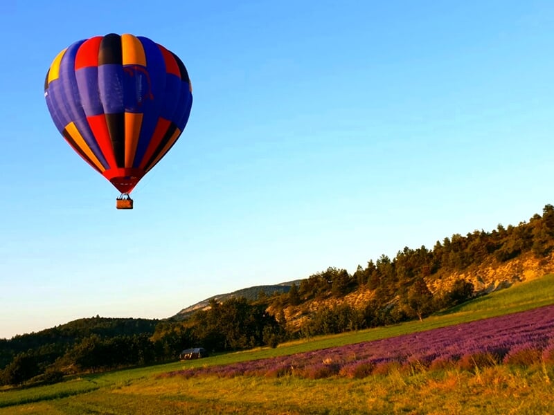 Montgolfière colorée flottant au-dessus d'un champ de lavande violet au pied de collines boisées.