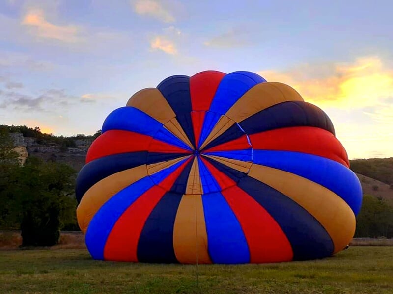 Montgolfière partiellement dégonflée reposant dans une prairie au coucher du soleil.
