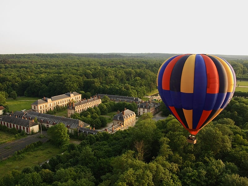 Vue aérienne d'une montgolfière flottant au-dessus du château de Fontainebleau entouré d'une forêt dense.
