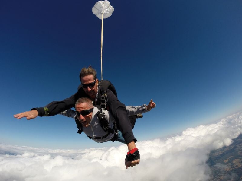 Deux personnes en chute libre lors d'un saut en parachute au-dessus des nuages avec un ciel bleu clair en arrière-plan.