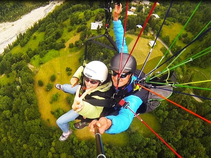 Un moniteur de parapente prend une photo en plein vol biplace à l'aide d'une perche à selfie.