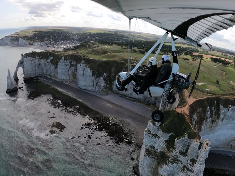 Petit avion ULM en vol au-dessus d'un paysage rural avec des champs et des arbres