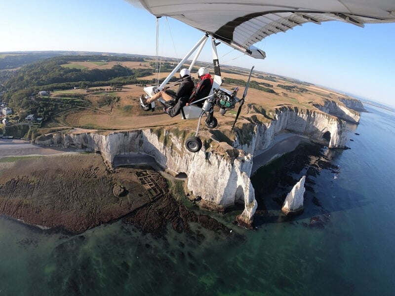 Avion ULM en vol au-dessus d'un paysage rural avec des champs et des arbres verts