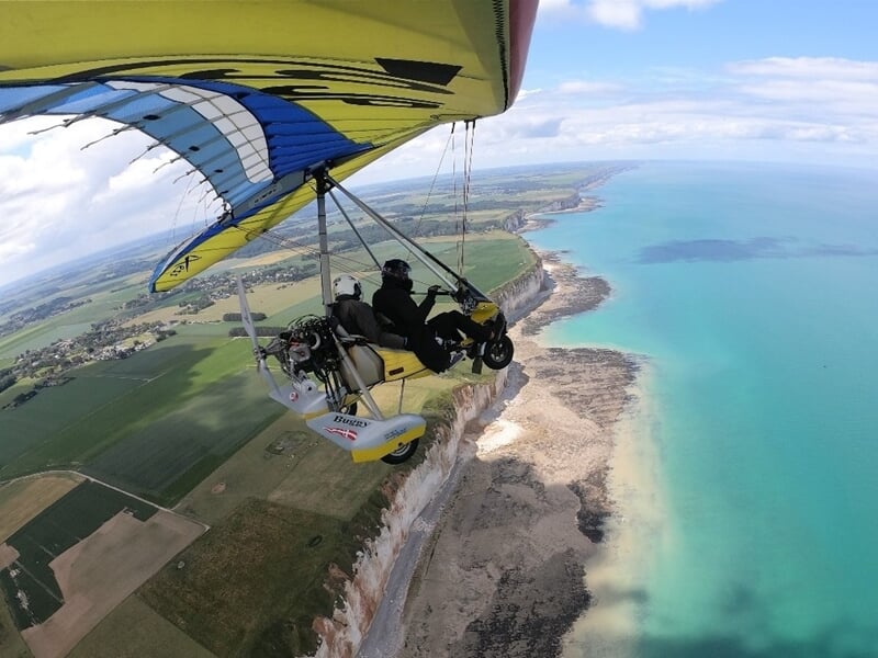 Petit avion ULM en vol au-dessus d'un paysage rural avec des champs et des arbres
