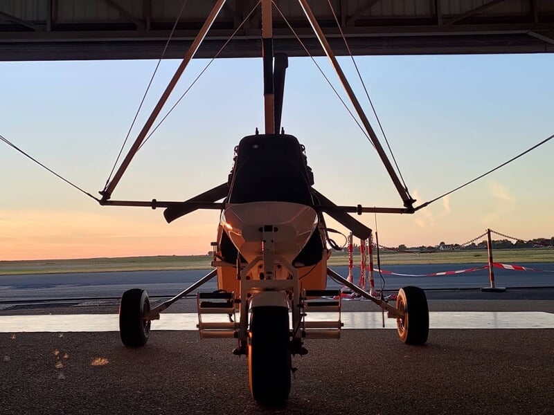 Avion ULM en vol au-dessus d'un paysage rural avec des champs et des arbres verts