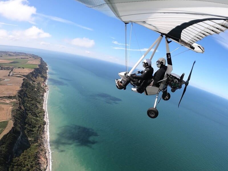 Petit avion ULM en vol au-dessus d'un paysage rural avec des champs et des arbres