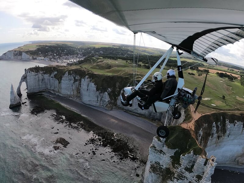Avion ULM en vol au-dessus d'un paysage rural avec des champs et des arbres verts