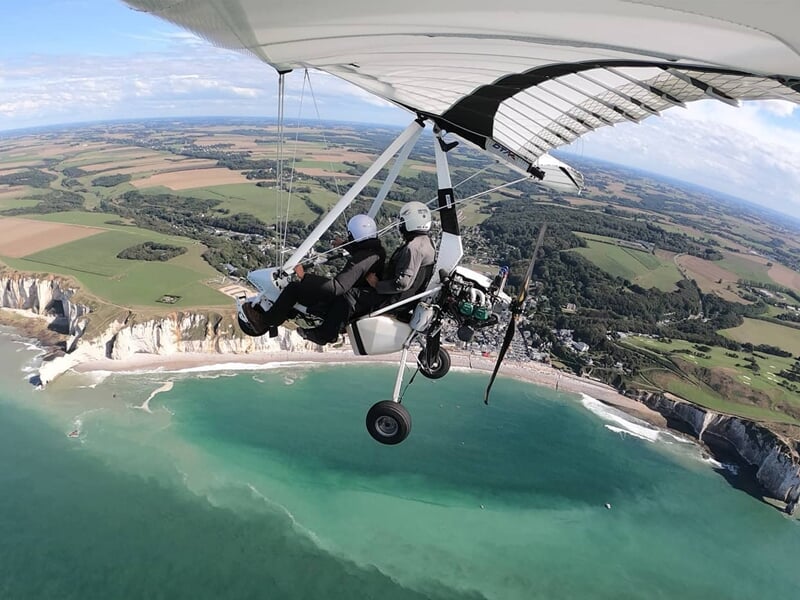Petit avion ULM en vol au-dessus d'un paysage rural avec des champs et des arbres