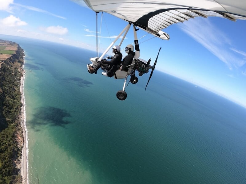 Avion ULM en vol au-dessus d'un paysage rural avec des champs et des arbres verts