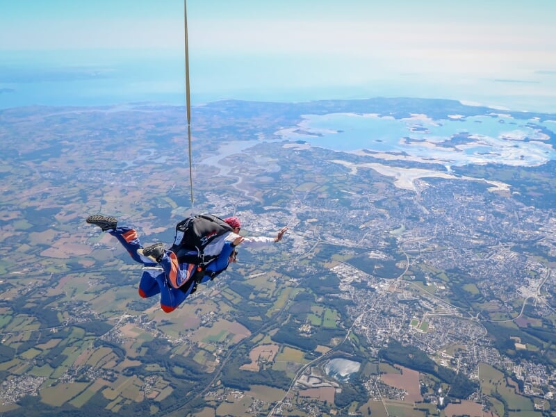 Vue aérienne de parachutiste en solo en position de vol horizontal, au-dessus du paysage urbain avec rivières et champs, parachute replié dans le dos, vêtements de saut bleu et rouge, sensation de hau