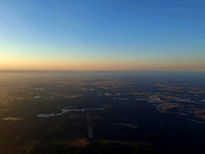 Montgolfière colorée survolant un paysage rural avec des champs et des collines vertes