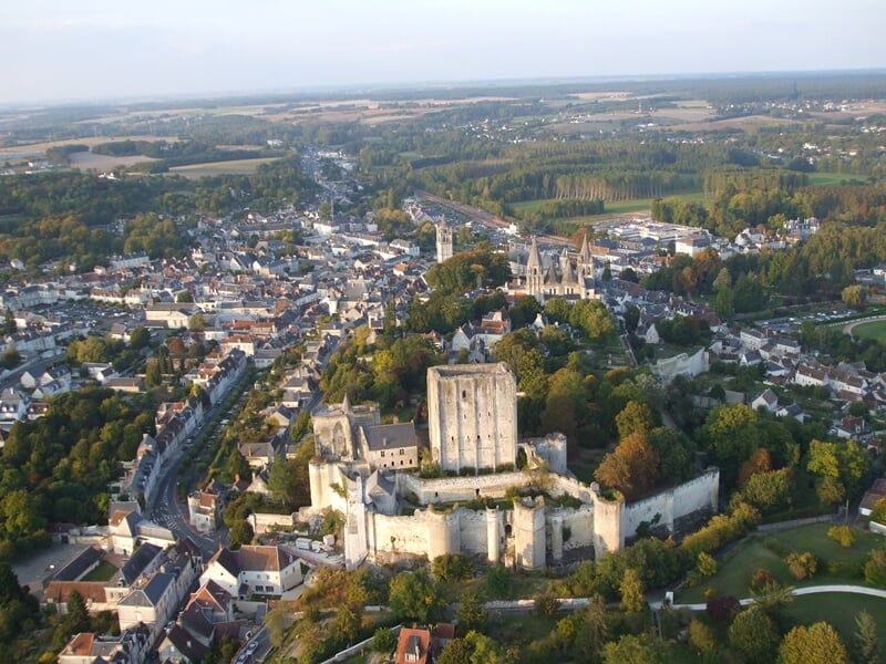 Montgolfière colorée survolant un village médiéval perché sur une colline au coucher du soleil