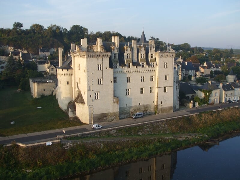 Montgolfière colorée survolant un village médiéval perché sur une colline au coucher du soleil
